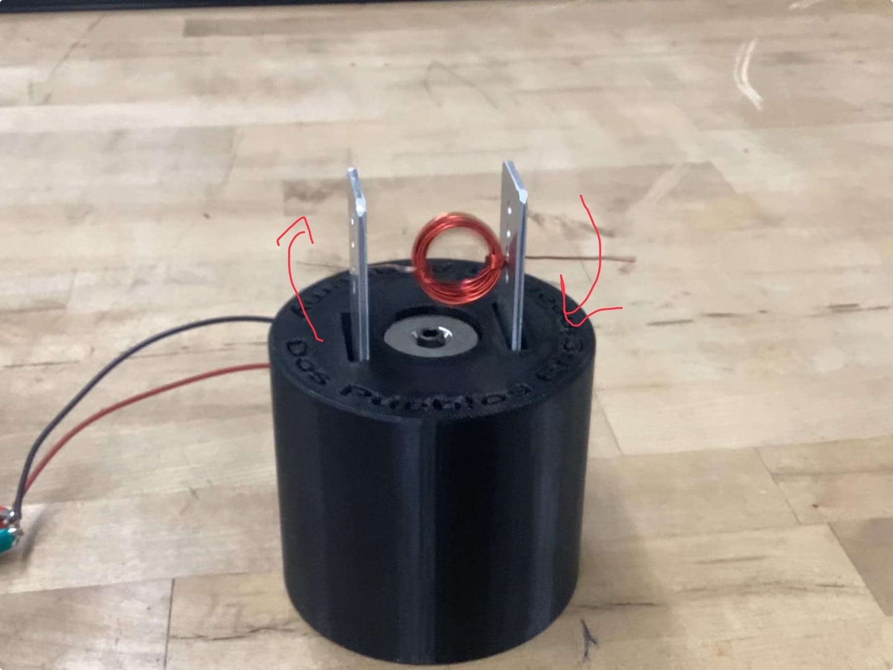 Simple electromagnetic motor experiment: a coil above a magnet in a black cylindrical stand.