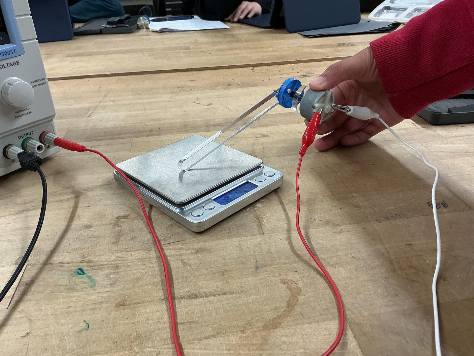 Bench setup with a power supply, a small motor and a digital scale measuring motor load.