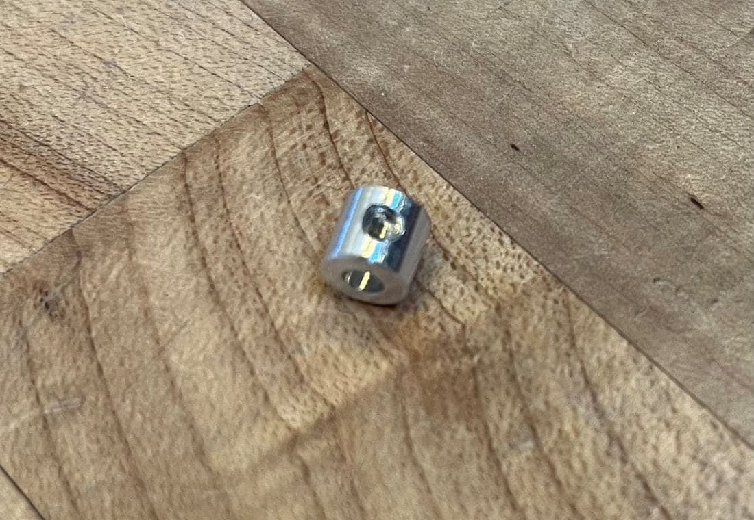 Small polished aluminum cylinder on a maple bench, with a drilled center hole in its end and a set screw in a tapped hole on its side.