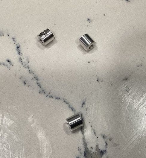 Three small bored aluminum cylinders of equal length lying on a white veined countertop.