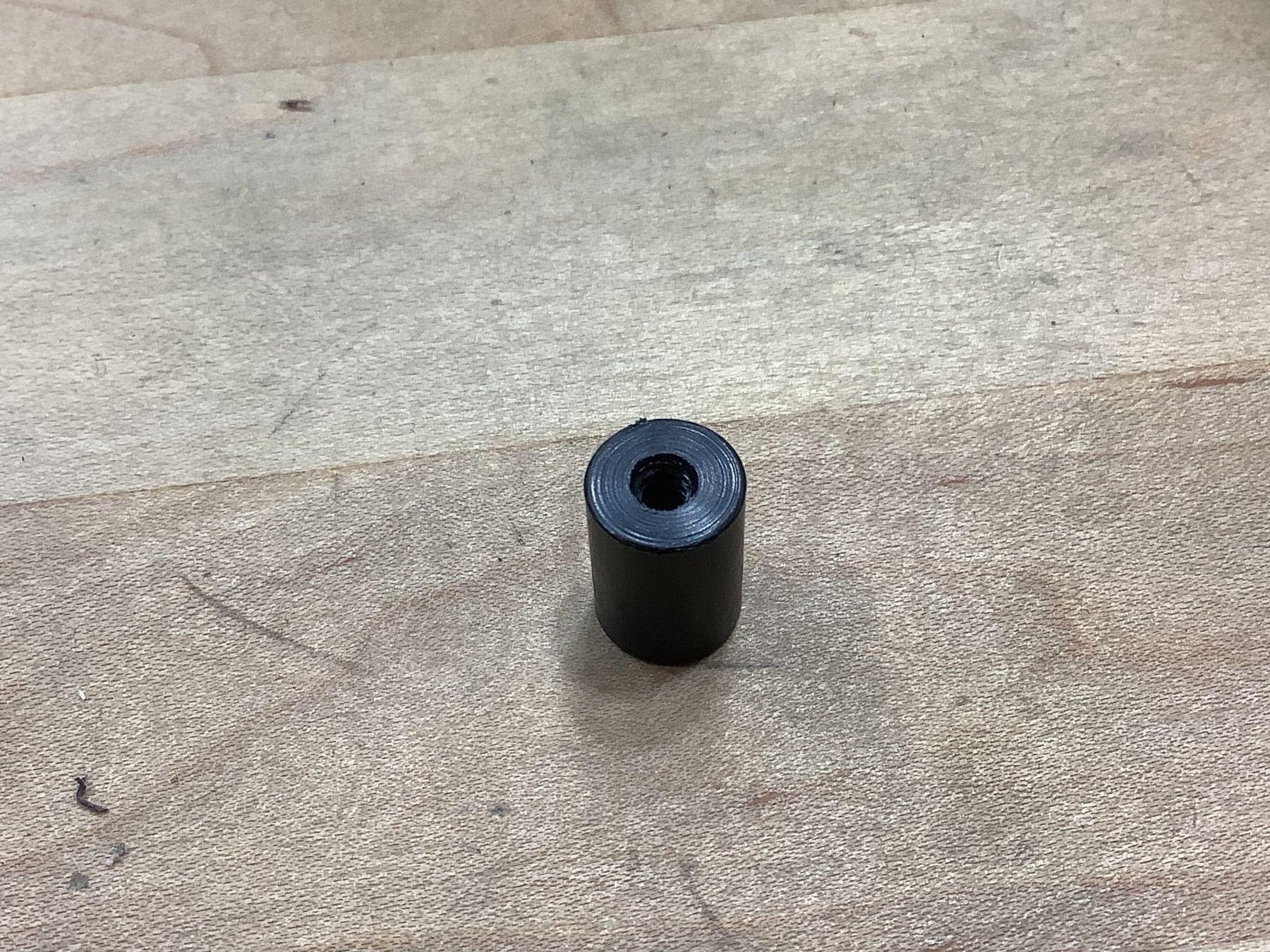 Close-up of a machined black spacer standing on a wood bench, its tapped bore visible.