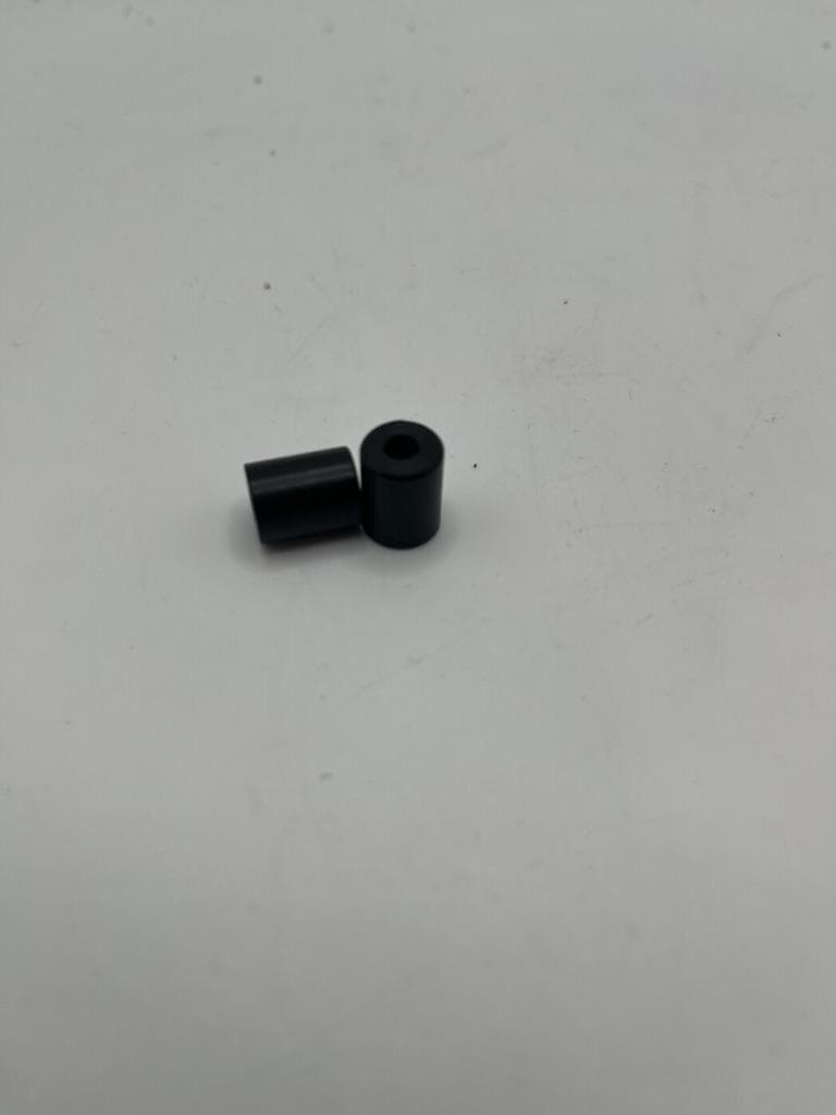 Two machined black Delrin spacers, one standing and one on its side.
