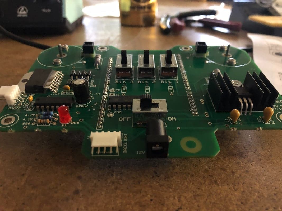 Green populated circuit board on a workbench with three slide switches labeled Bit 3, Bit 2, Bit 1, an OFF/ON switch, a black heatsink and a red LED.