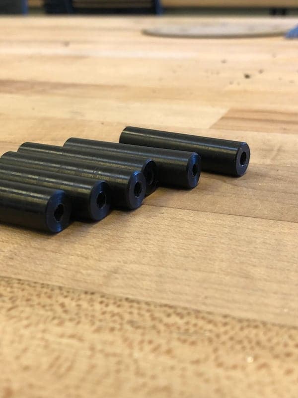 Six black cylindrical plastic spacers lying side by side on a wooden bench, their threaded center holes facing the camera.