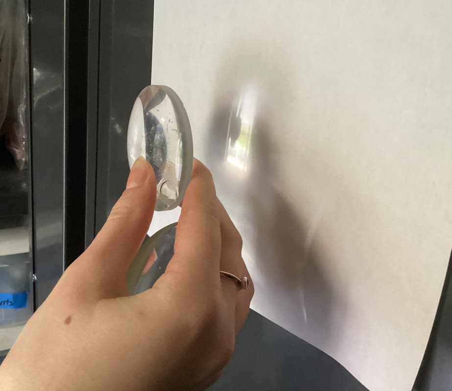 A hand holding lenses that project a small refracted image of a window onto white paper.