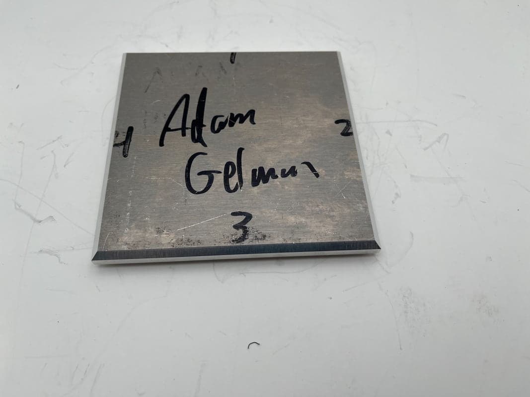 Square aluminum plate with beveled edges, hand-marked Adam Gelman and numbered 1 to 4 on its sides.