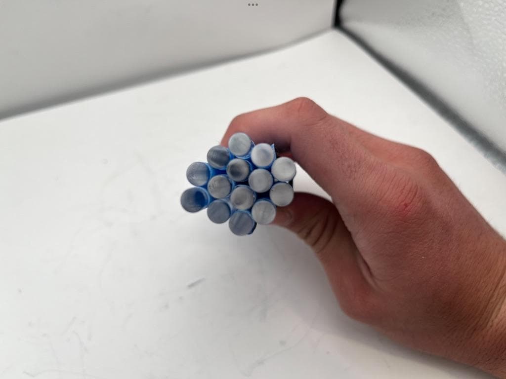 A hand holding a bundle of finished acrylic rods, seen end-on, against a white background.
