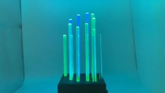 The finished Light Sculpture glowing teal and green: a field of acrylic rods of different heights rising from a black machined base.
