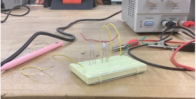 Breadboard with two small LEDs, resistors and jumper wires connected to a bench power supply.