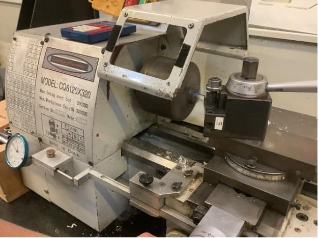 Benchtop manual lathe with a small part in the chuck and a tool post beside it.