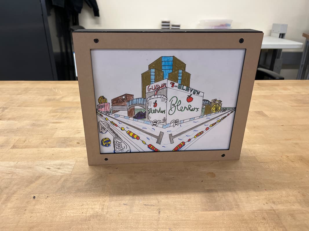 The finished shadow box standing on a bench, showing a colored two-point perspective city drawing in its frame.