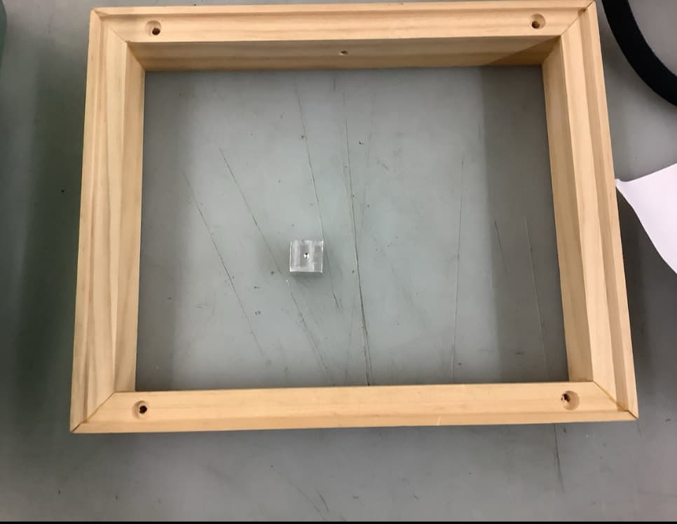 Unfinished mitered wood frame lying flat, with a hole drilled near each corner.